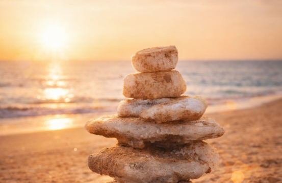 Ein harmonischer Steinturm am Strand bei goldenem Sonnenuntergang, der Balance, Achtsamkeit und innere Ruhe symbolisiert.